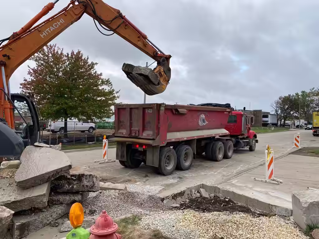 Excavator loading broken concrete slab into a Donegal Services dump truck during demolition work in Bensenville, IL.