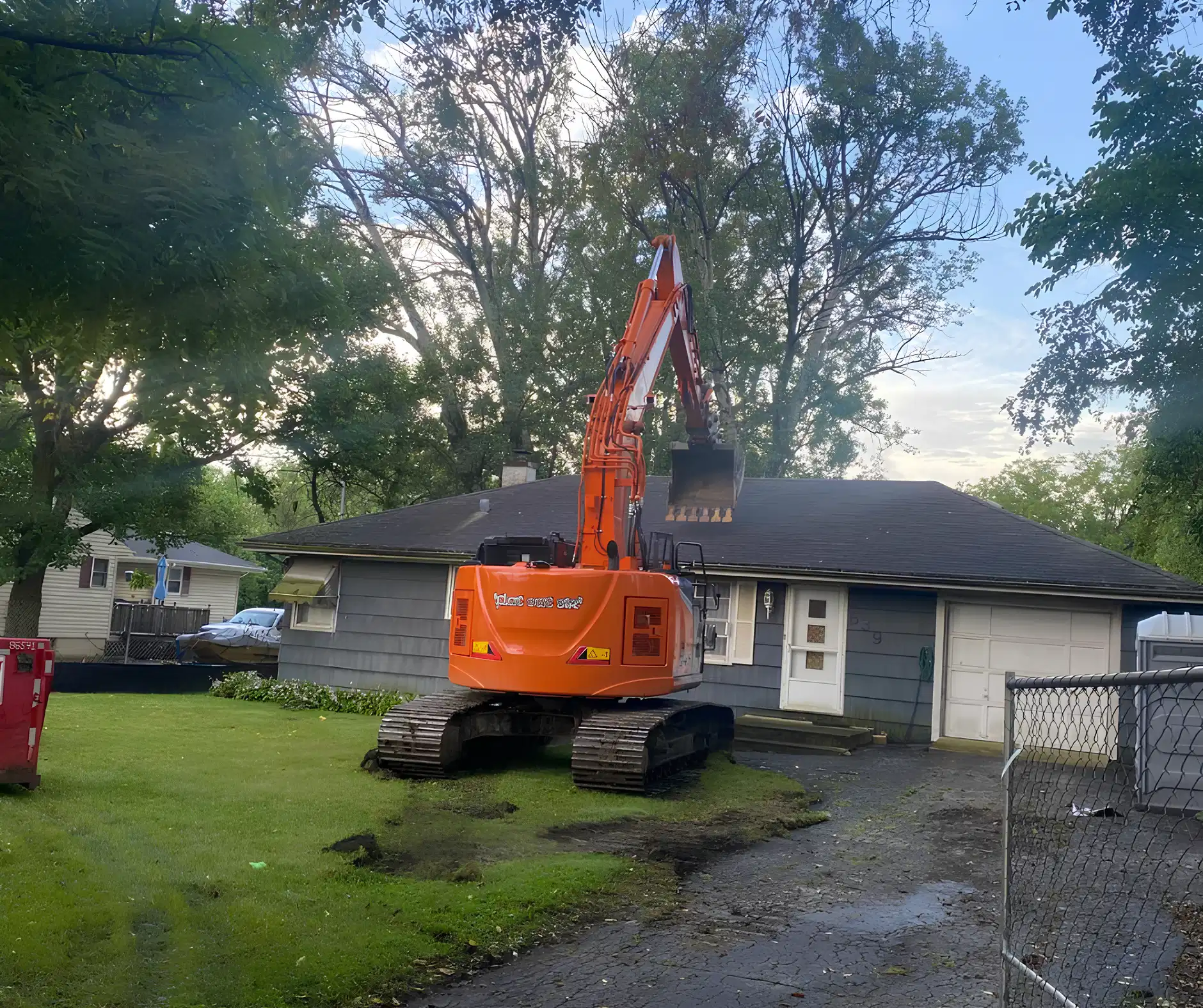 Orange excavator positioned for residential demolition at a single-family home, part of full tear-down services by Donegal Services in Chicagoland.
