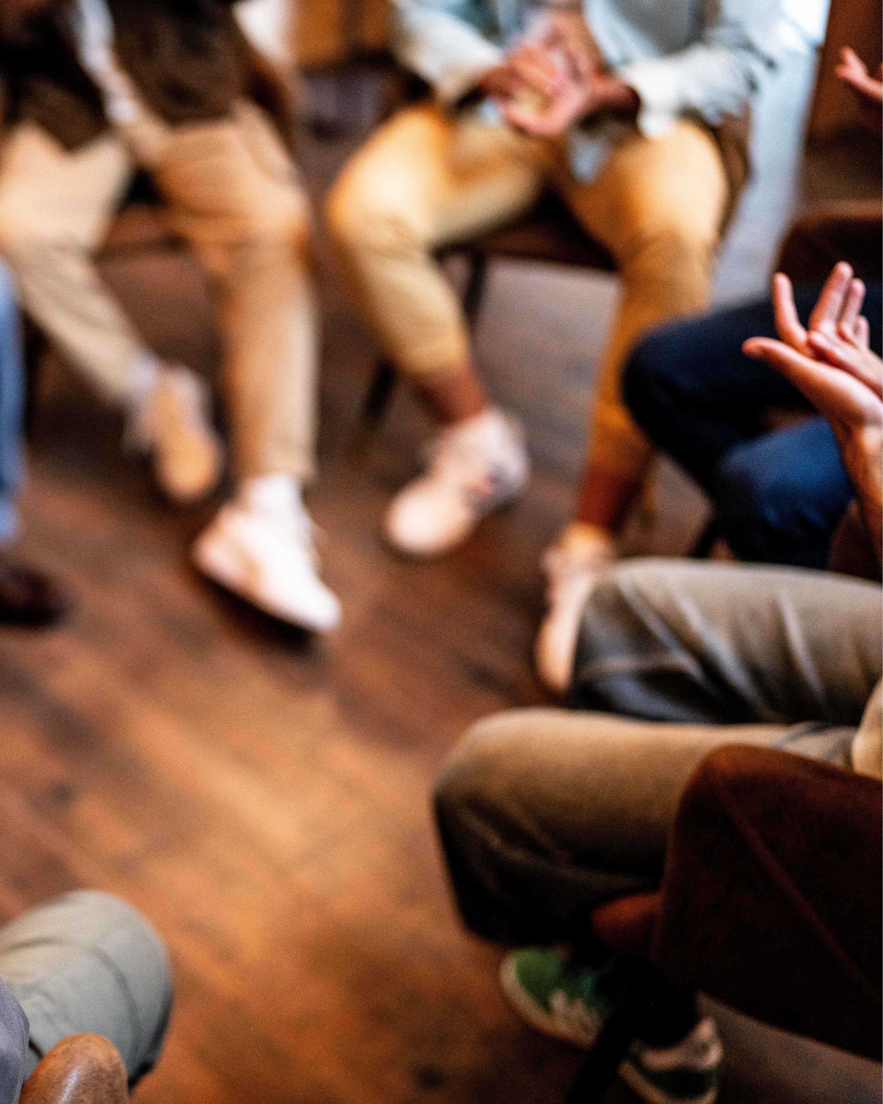 Group of people sitting in a circle on chairs, engaged in conversation with visible hand gestures.
