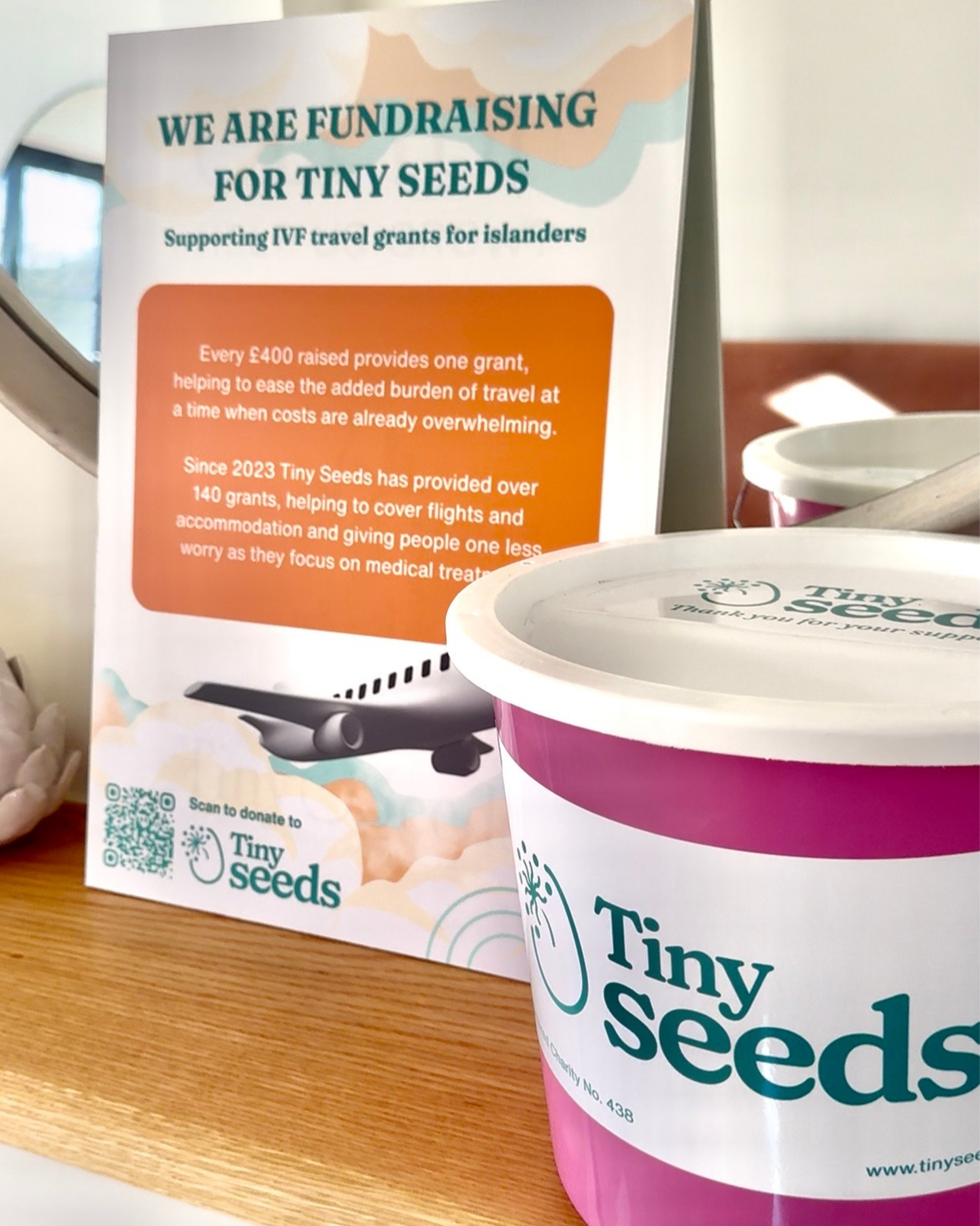Donation collection bucket and flyer for Tiny Seeds fundraising supporting IVF travel grants for islanders.