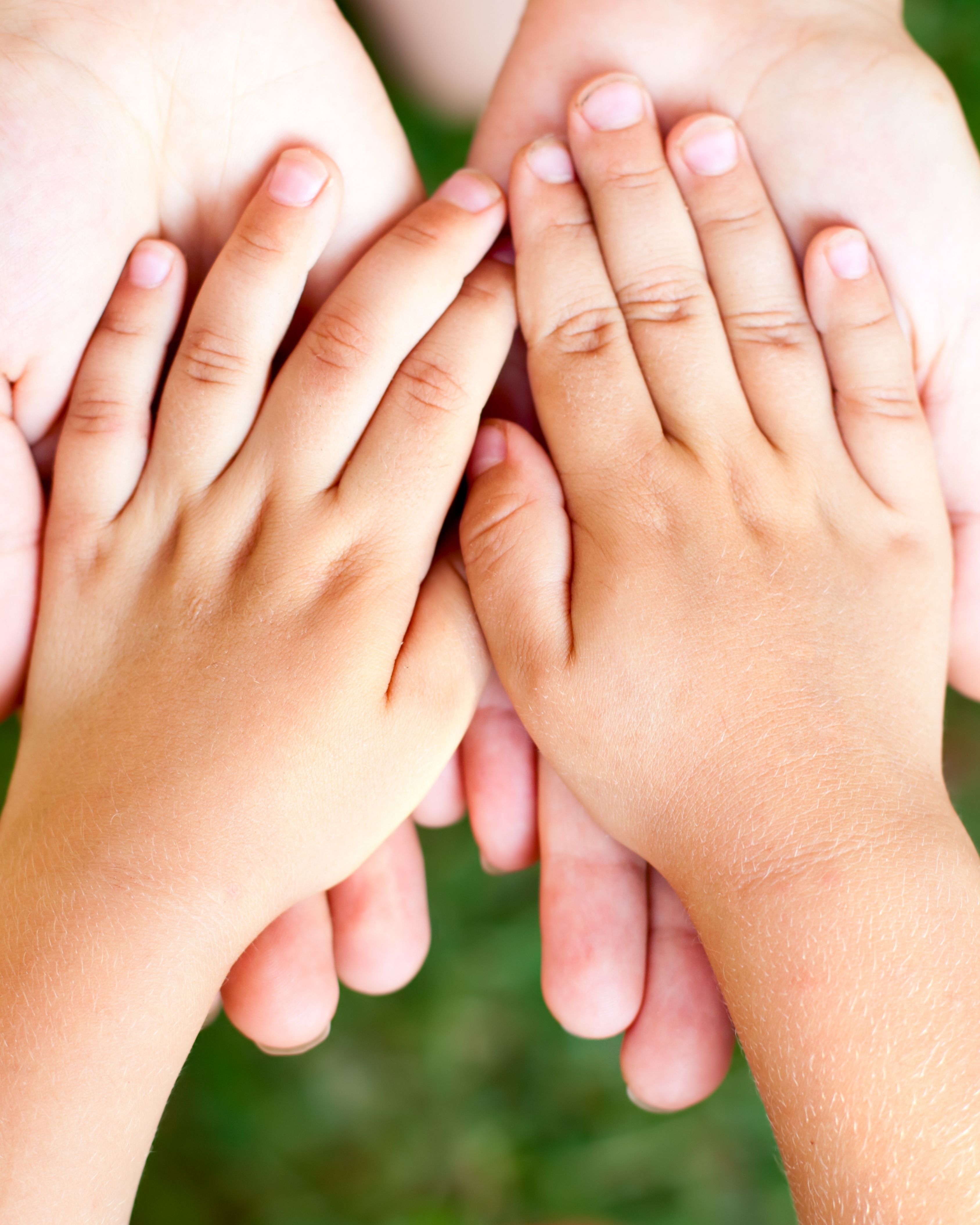 Two small child hands placed palm down over two adult hands palm up against a blurred green background.