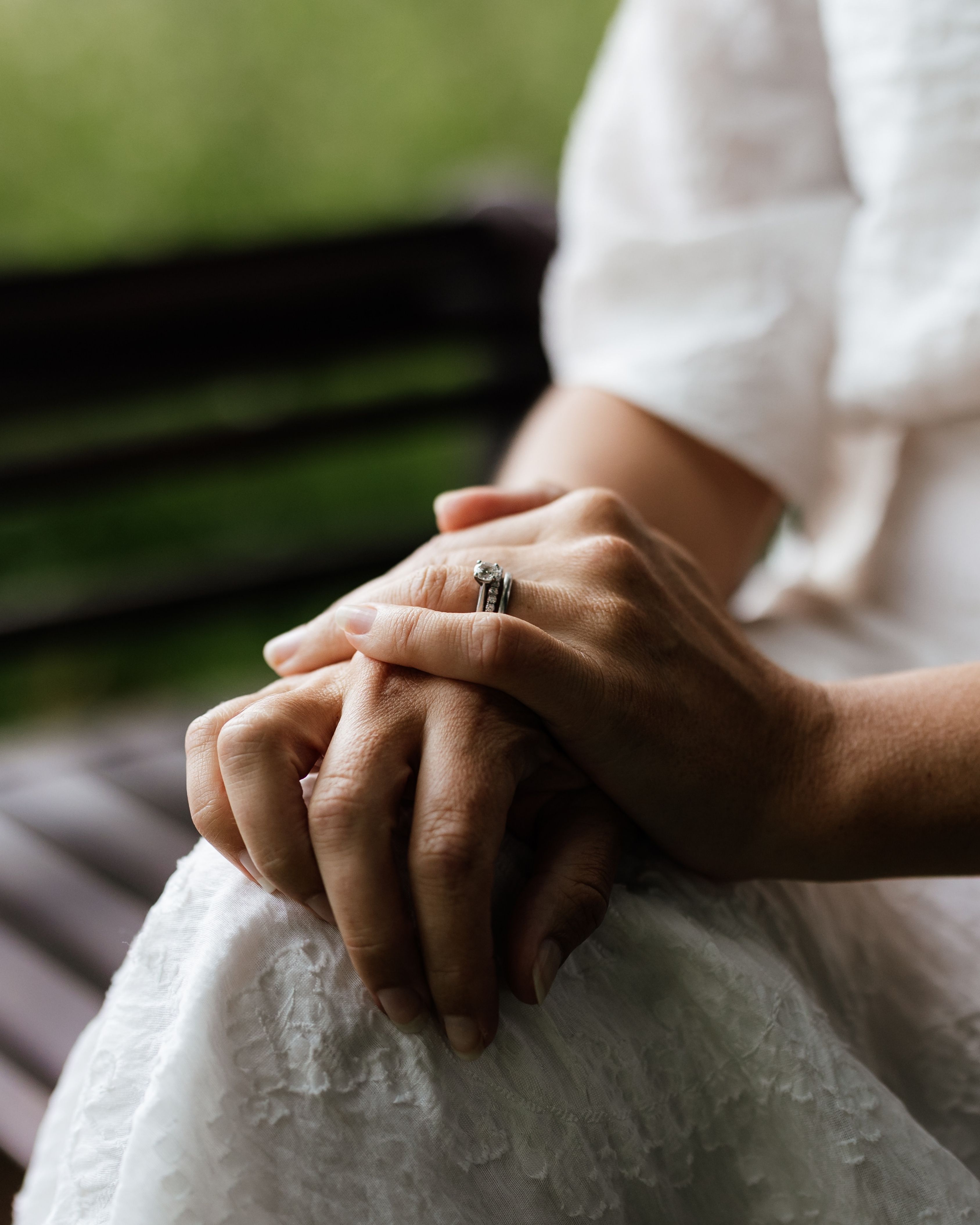 Woman’s hands resting on her lap, wearing a silver engagement ring with a diamond.