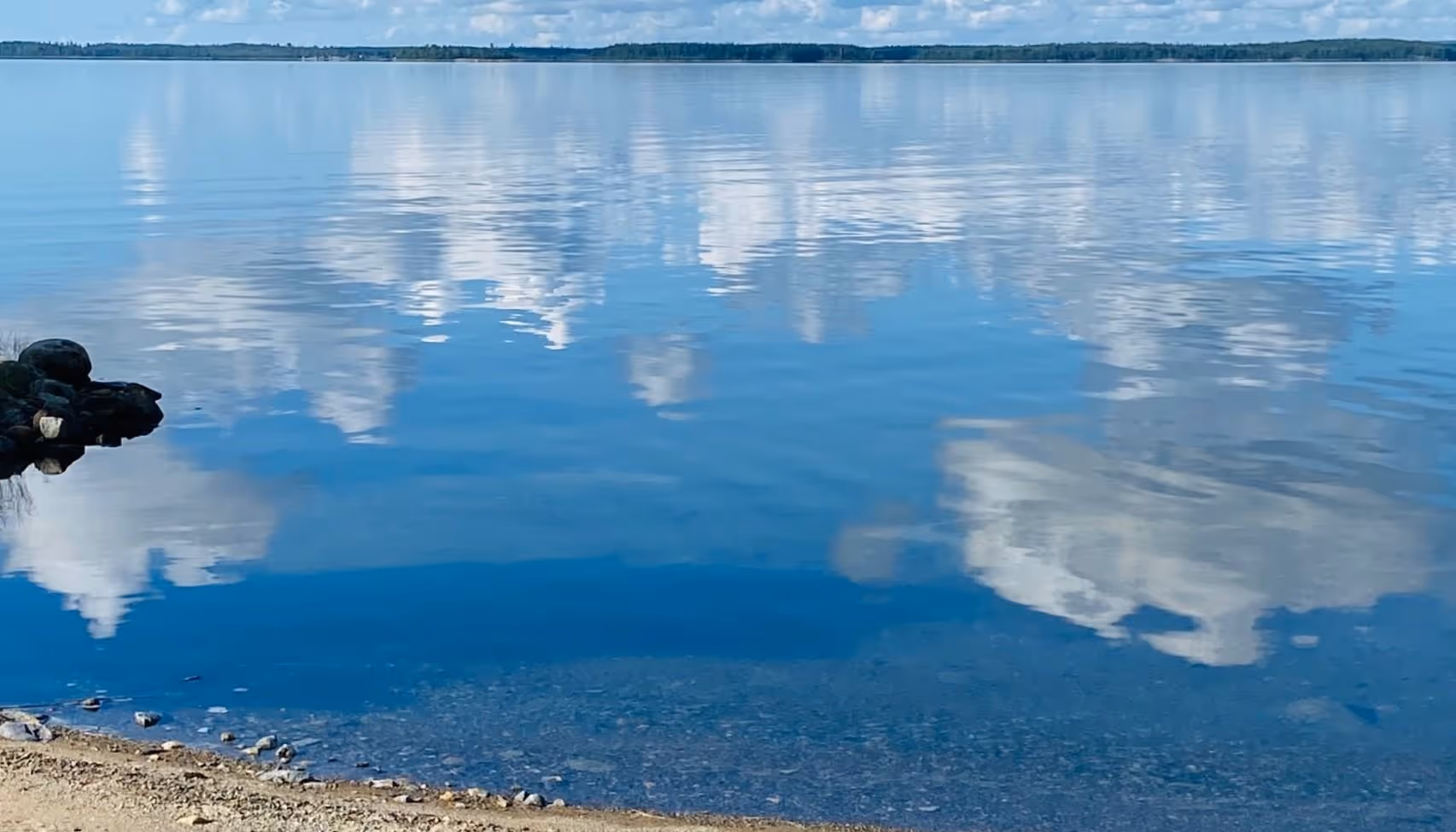Spegelblankt vatten med blå himmel och vita moln som speglas i ytan, en rofylld naturmiljö som symboliserar lugn och balans – värden som Vigilans Umeå AB vill hjälpa personer med ADHD att nå i sin vardag.