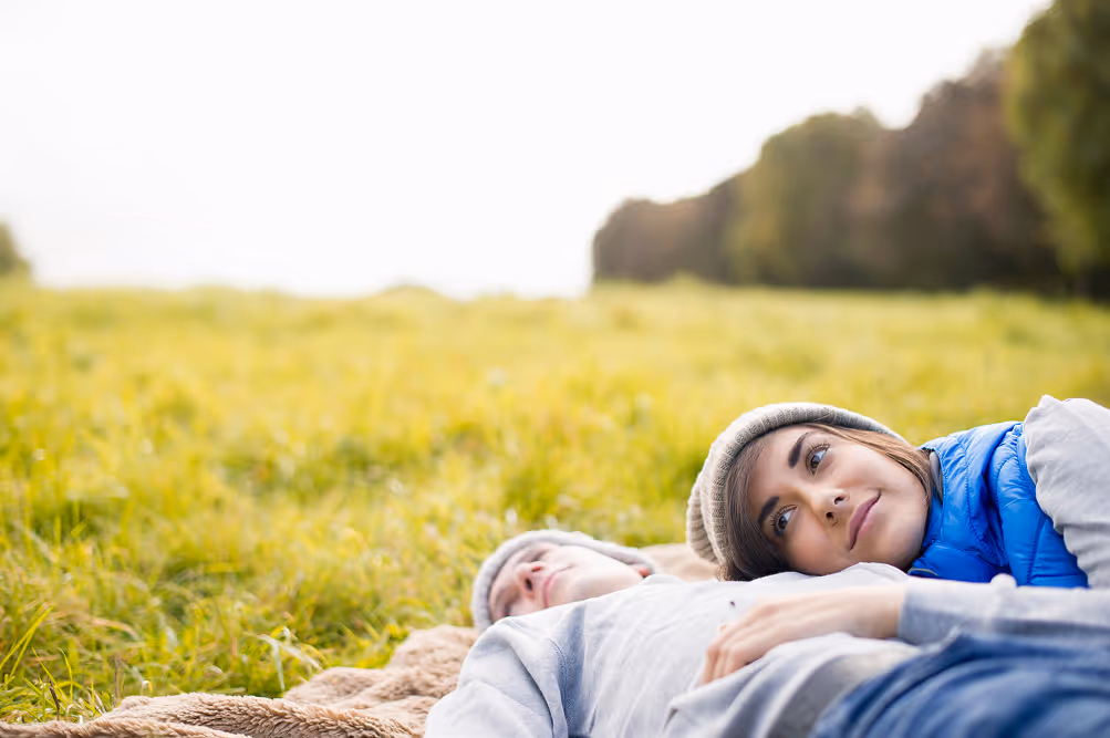 Två personer ligger avslappnat på en filt i gräset, vilket uttrycker vila och trygghet – värden som Vigilans Umeå AB vill hjälpa sina patienter att nå i sin vardag.