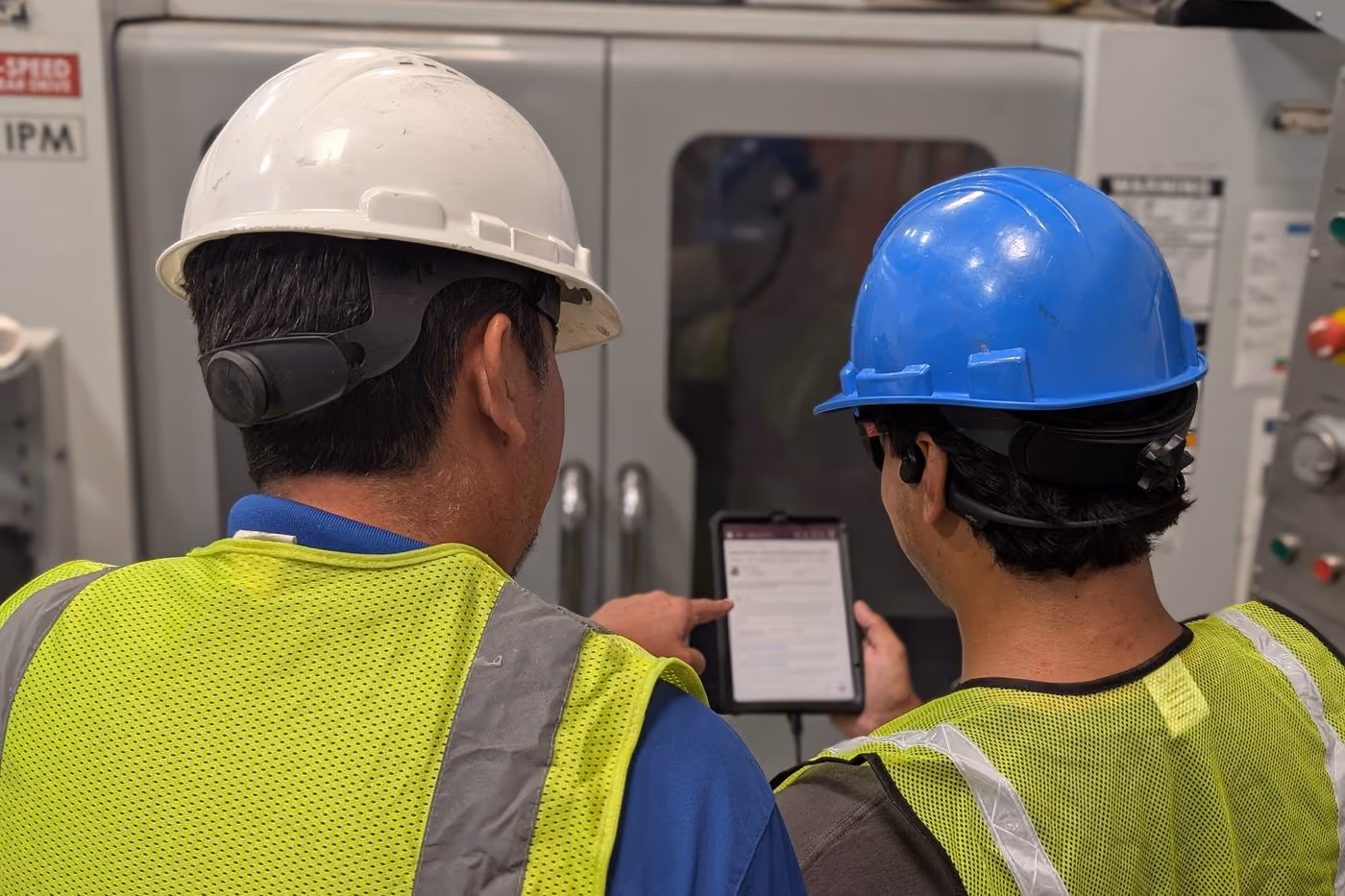 An experienced technician showing a colleague a procedure on a tablet at a machine