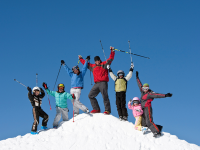 Groupe de six personnes, dont des enfants, debout et célébrant au sommet d'une colline de neige avec un ciel bleu clair en arrière-plan.