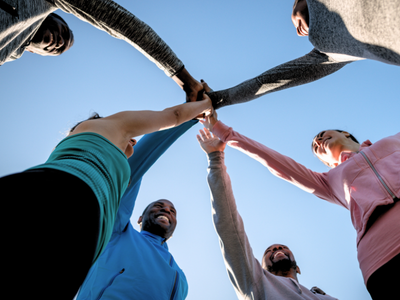 Groupe de personnes se tenant la main en cercle sous un ciel bleu clair.