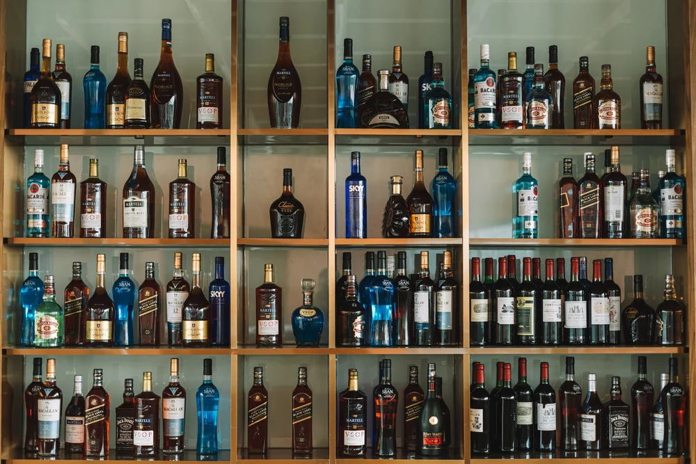 Wooden shelves filled with various bottles of liquor, including whiskey, vodka, and wine, arranged in neat rows.
