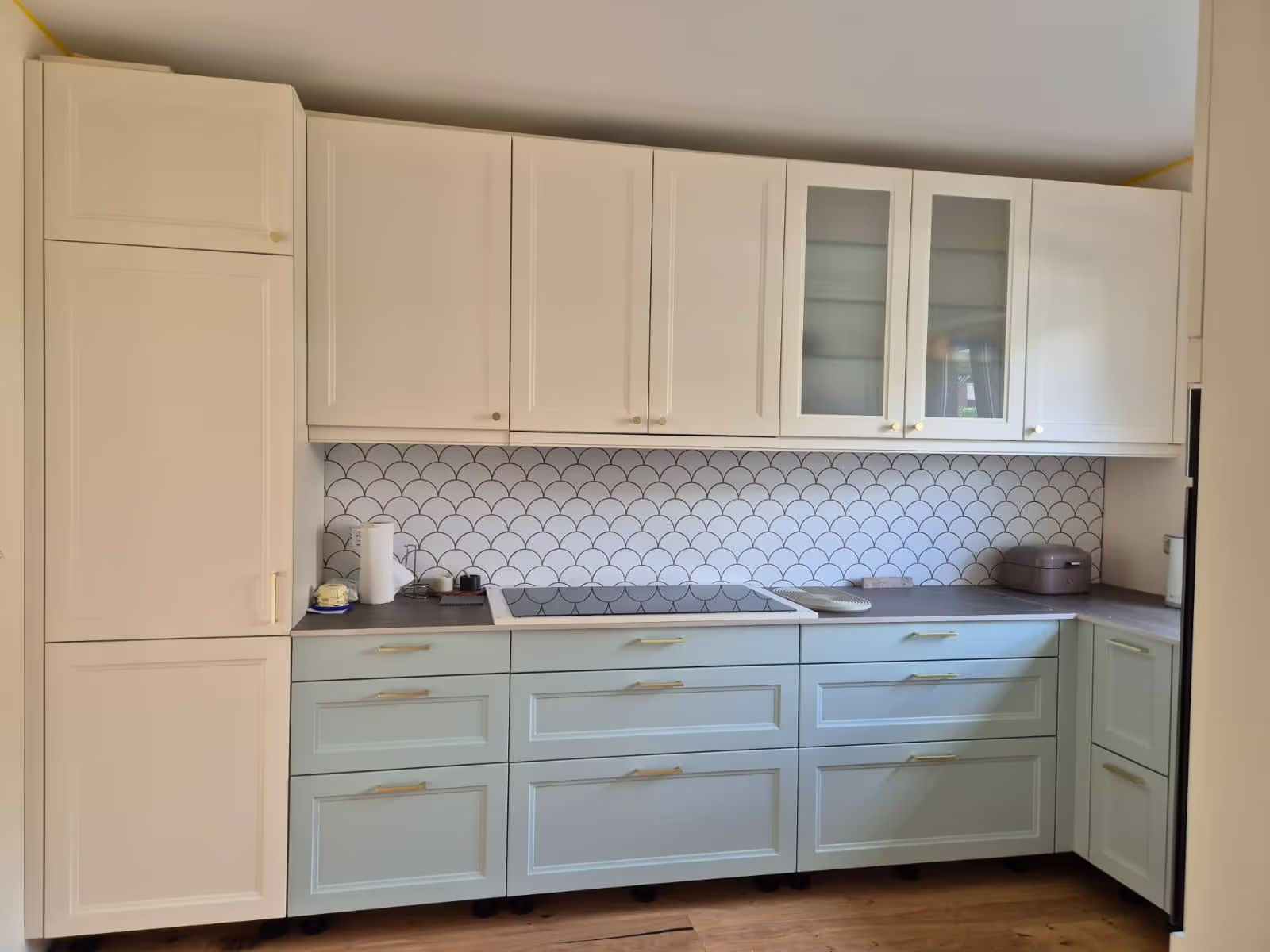 Modern kitchen with cream upper cabinets, light blue lower drawers, black countertop, and a white tiled backsplash with a scallop pattern.