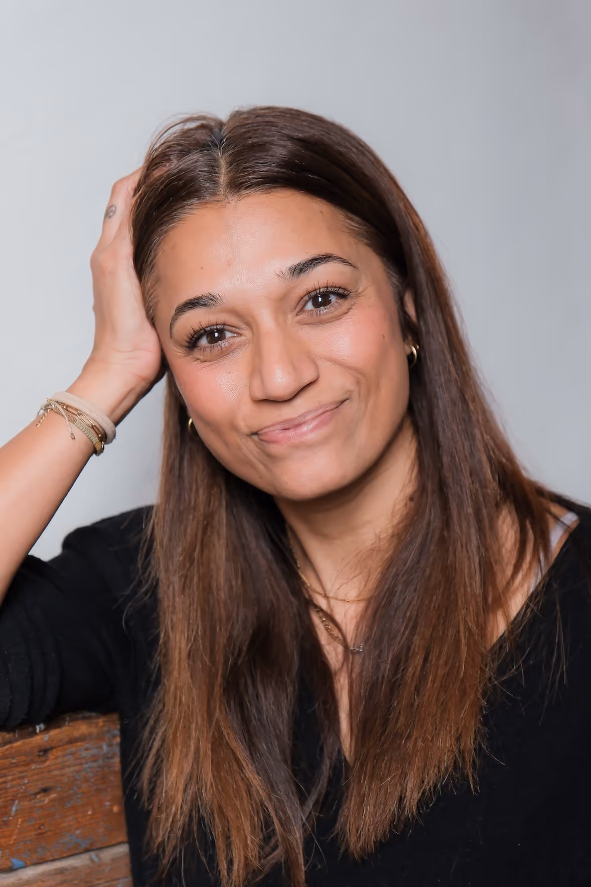 Porträt einer lächelnden Frau mit braunen Haaren, die den Kopf mit der Hand stützt.