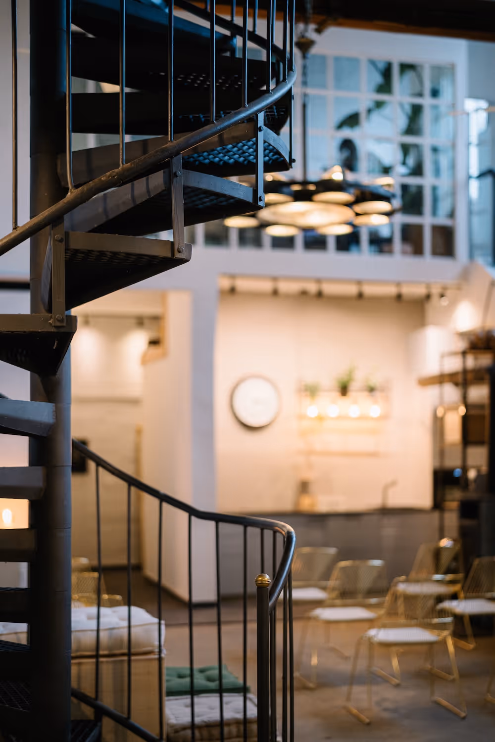 Schwarze Wendeltreppe in einem modernen Raum mit Stühlen und einem großen Fenster im Hintergrund.