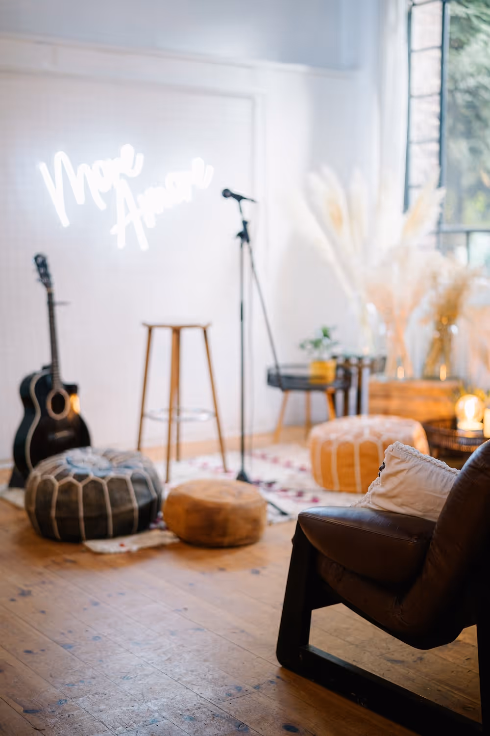 Gemütlicher Raum mit Mikrofonständer, Akustikgitarre und Sitzkissen auf Holzboden vor weißer Wand mit leuchtendem Schriftzug.