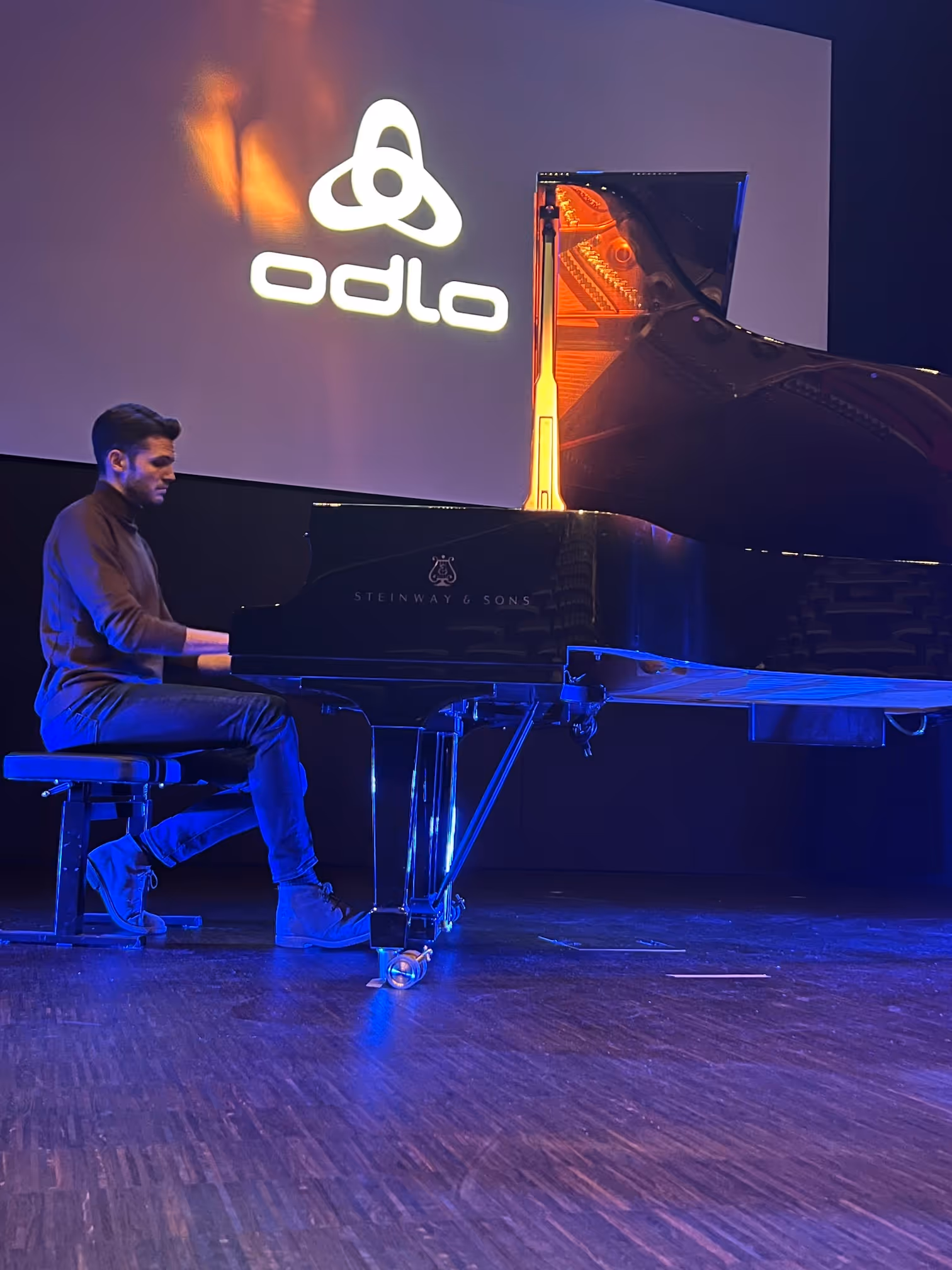 Ein Mann spielt Klavier auf einer Bühne mit einem großen Steinway & Sons Flügel, im Hintergrund das odlo-Logo.