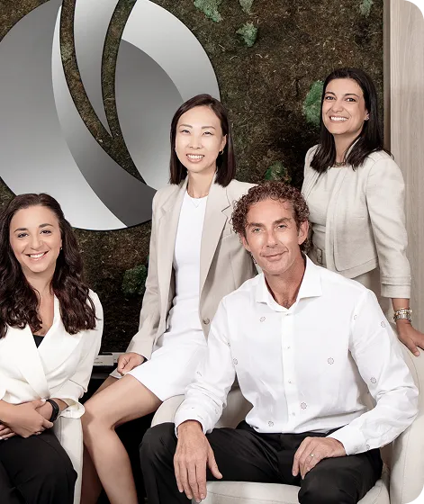 Group of four professionally dressed people smiling in an office setting with a green moss wall and a modern silver logo behind them.