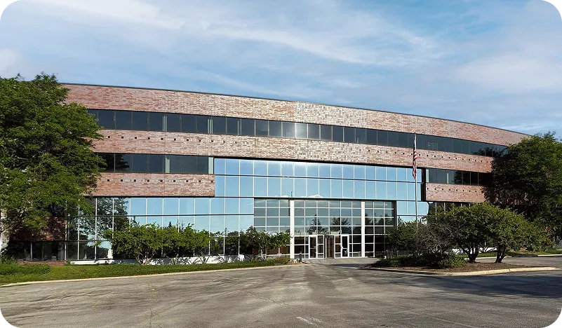 Modern three-story office building with large glass windows, brick facade, and an American flag on a flagpole in front.