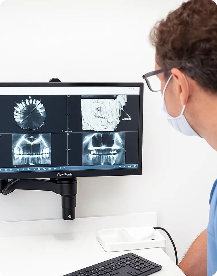 Dentist wearing a mask examining dental X-ray images displayed on a monitor in a clinic.