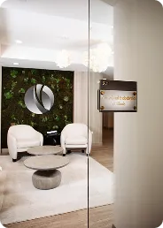 Modern office waiting area with two white armchairs, a circular coffee table, and a wall featuring a logo and green foliage.