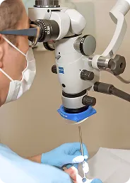 Medical professional wearing mask and gloves using a microscope for a precise procedure.