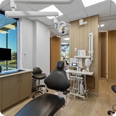 Modern dental examination room with a black dental chair, overhead light, dental instruments, and wood-paneled walls.