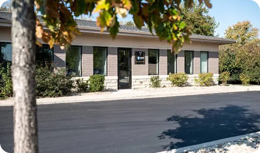 Single-story office building with brick and stone facade, surrounded by shrubs and trees.