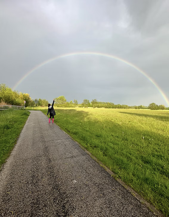 vrouw loopt in natuurgbied wijzend naar de regenboog