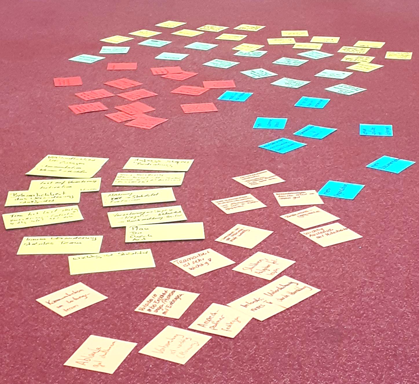 Colored sticky notes with handwritten text arranged in clusters on a red carpet floor.