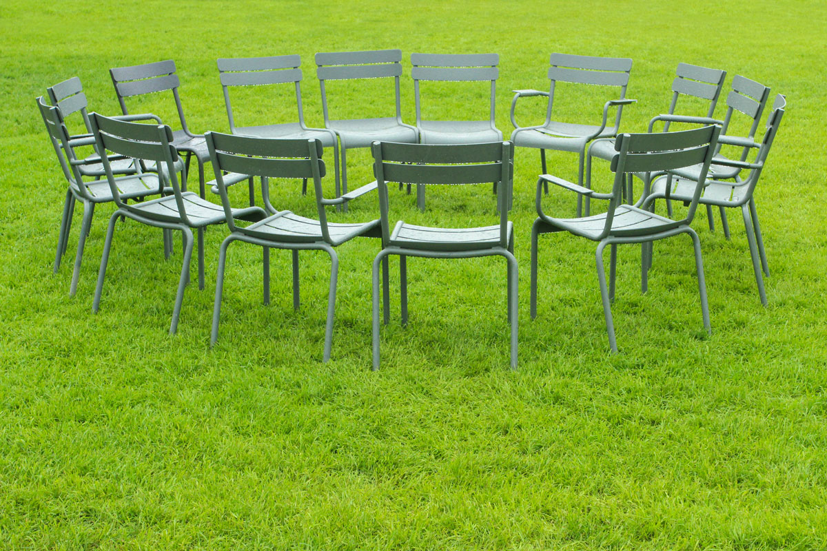 Circle of metal chairs arranged on green grass outdoors.