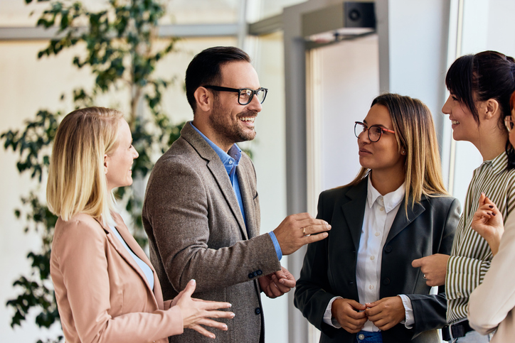 Four professionally dressed colleagues engaged in a friendly conversation in an office setting.