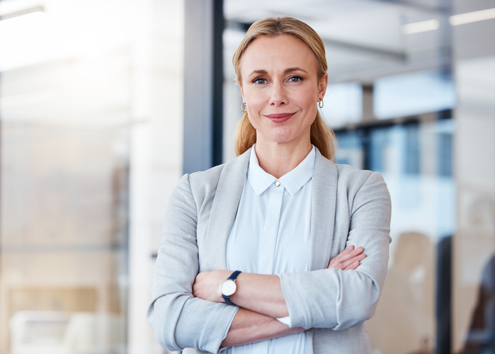 Confident businesswoman with arms crossed smiling in a modern office setting.