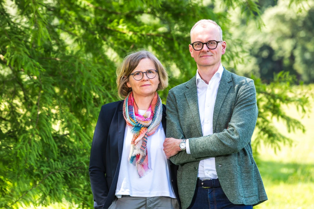 Portrait von Babara und Daniel die in die Kamera blicken. Im Hintergrund sind Bäume und und Wiese zu sehen.