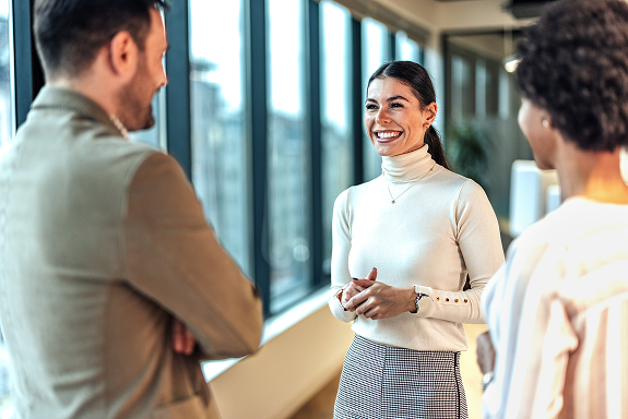 Tre kolleger i kontormiljø har en vennlig samtale ved vinduet.