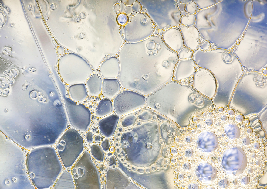 Nærbilde av gjennomsiktige bobler i et væskeblanding med blå og gule nyanser.