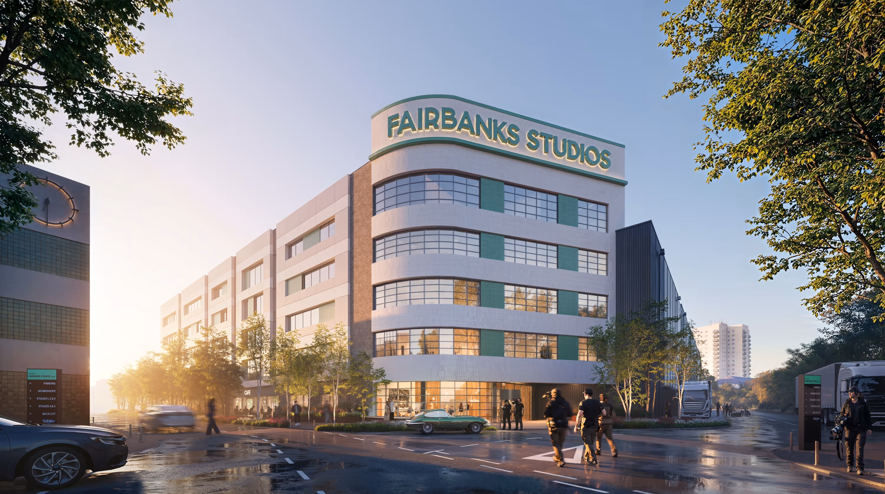 Modern Fairbanks Studios building with large windows at sunset, surrounded by trees, cars, and people on wet streets.