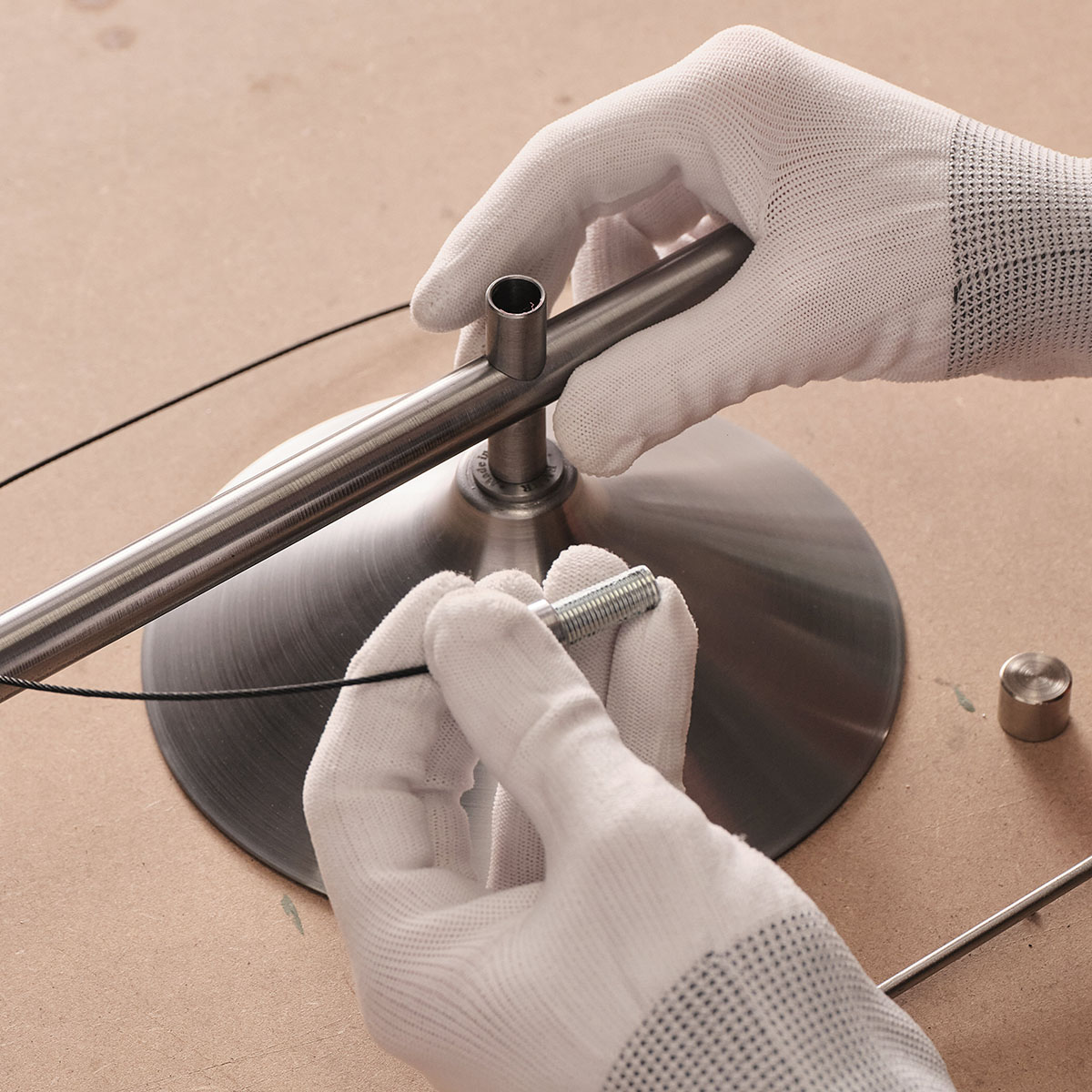 Gloved hands assembling the stem and base of a metal table lamp.