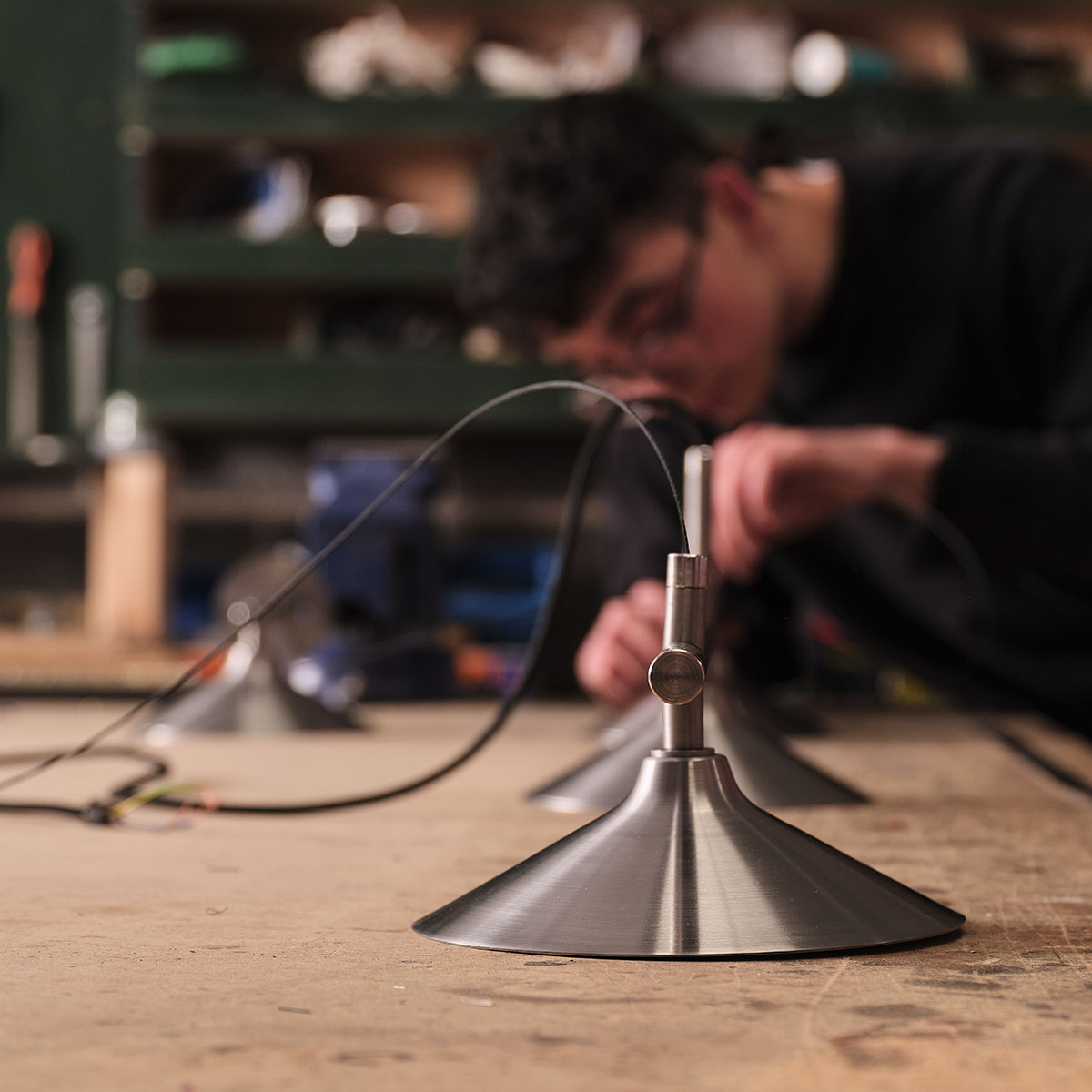 Craftsperson assembling a metal pendant light on a workshop bench.