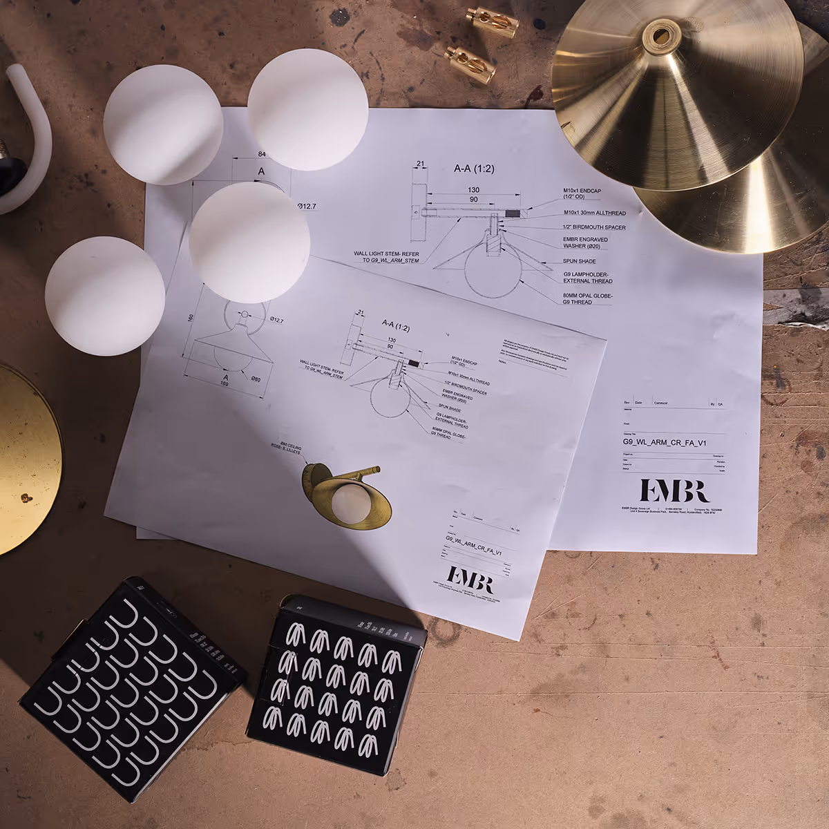 EMBR lighting drawings surrounded by bulbs, metal shades and finish samples.
