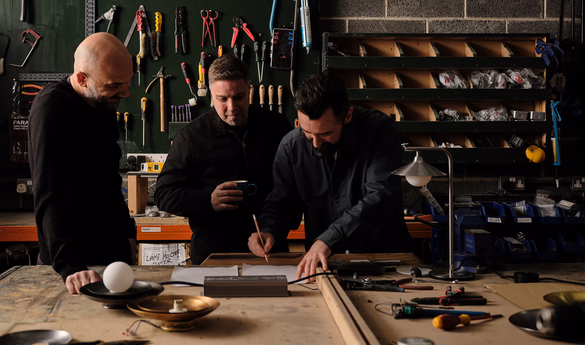 Three EMBR founders gathered around drawings and lighting components in the workshop.