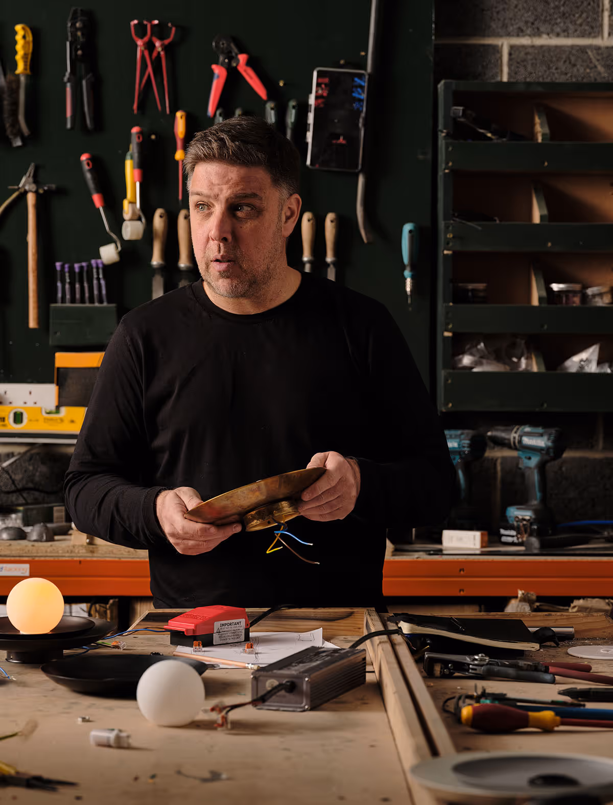 Chris holding a light component at a workshop bench.