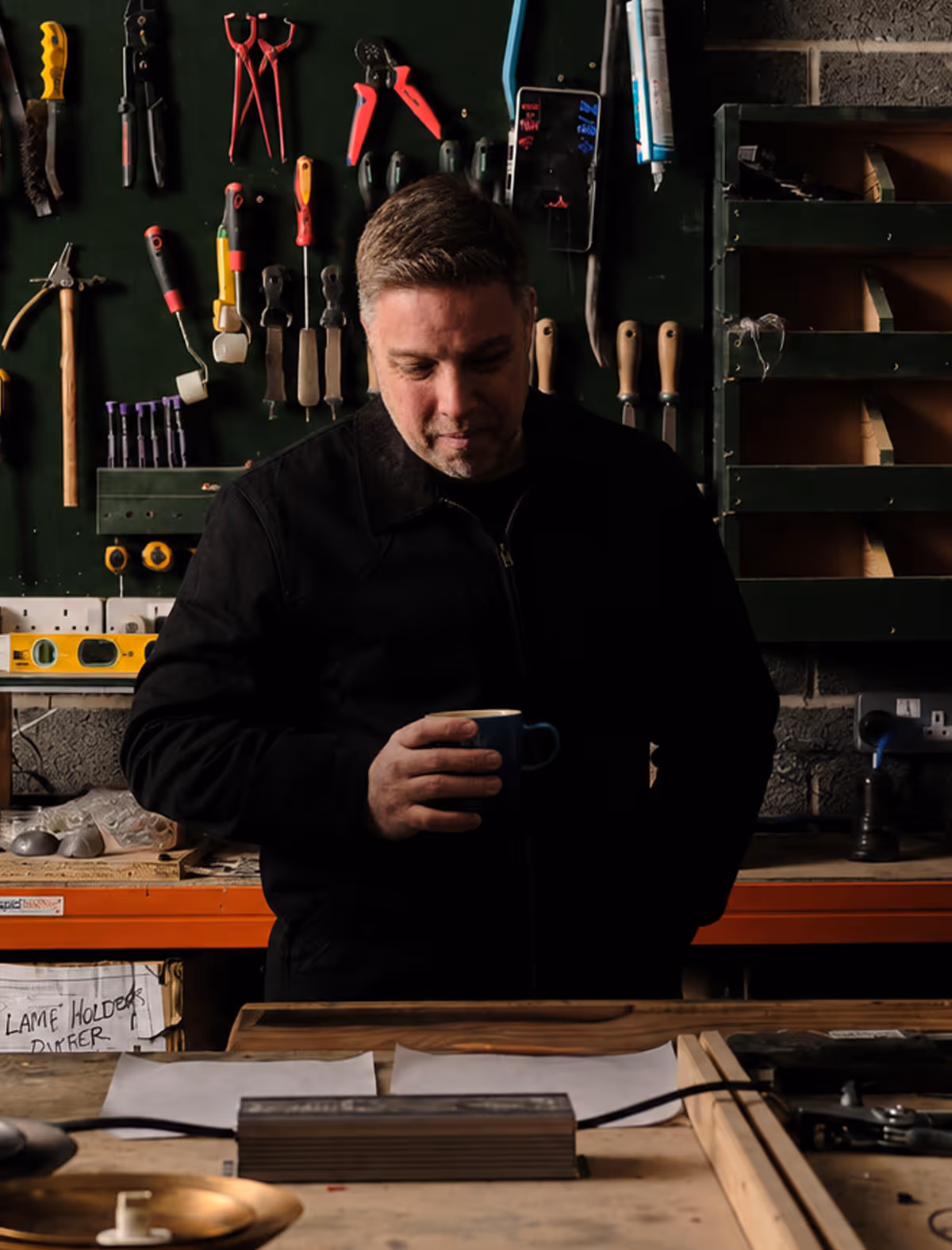 Chris standing at a workshop bench in front of a wall of hand tools.
