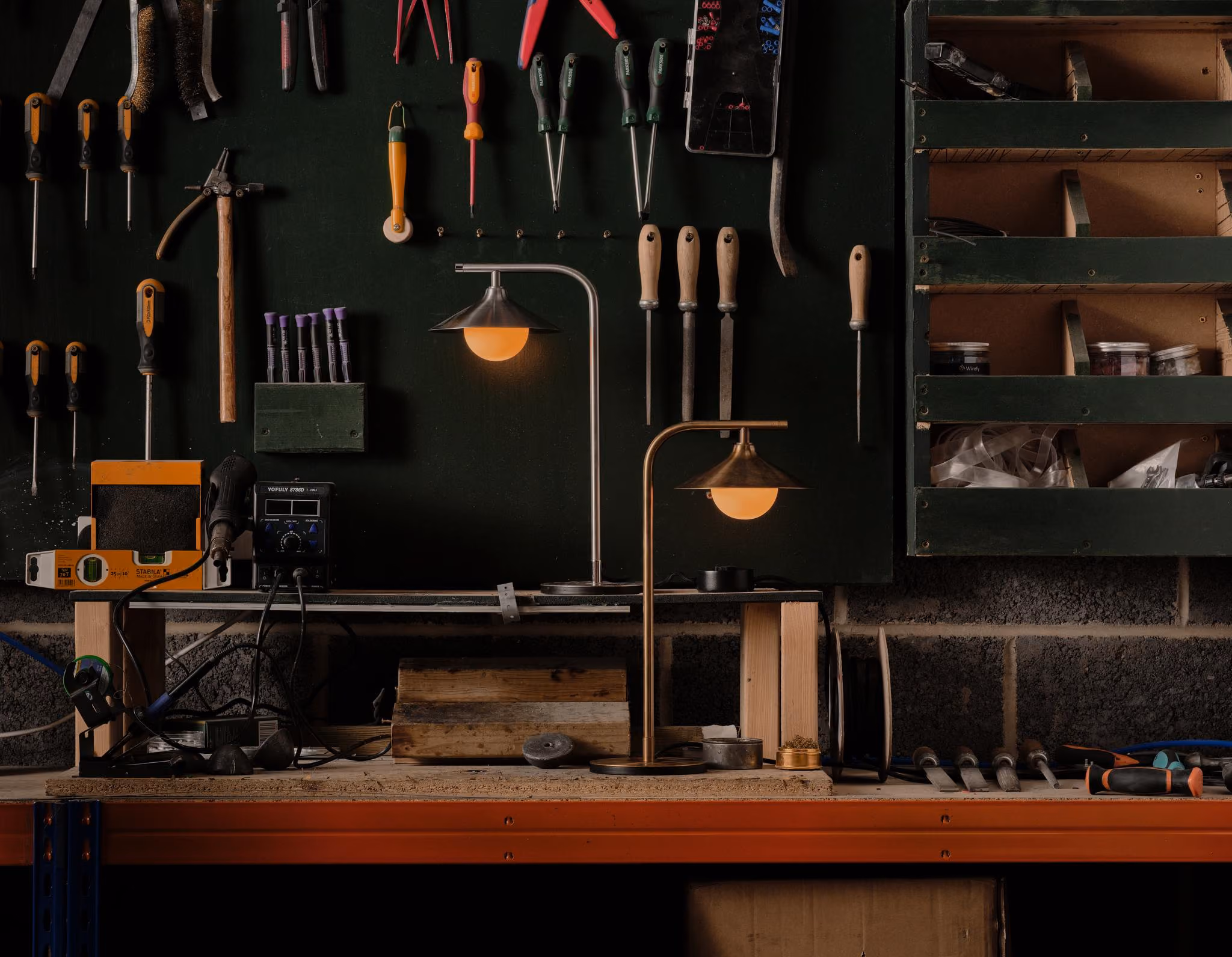 Two Mettle Alba table lamps glowing on a workbench beneath hanging tools.