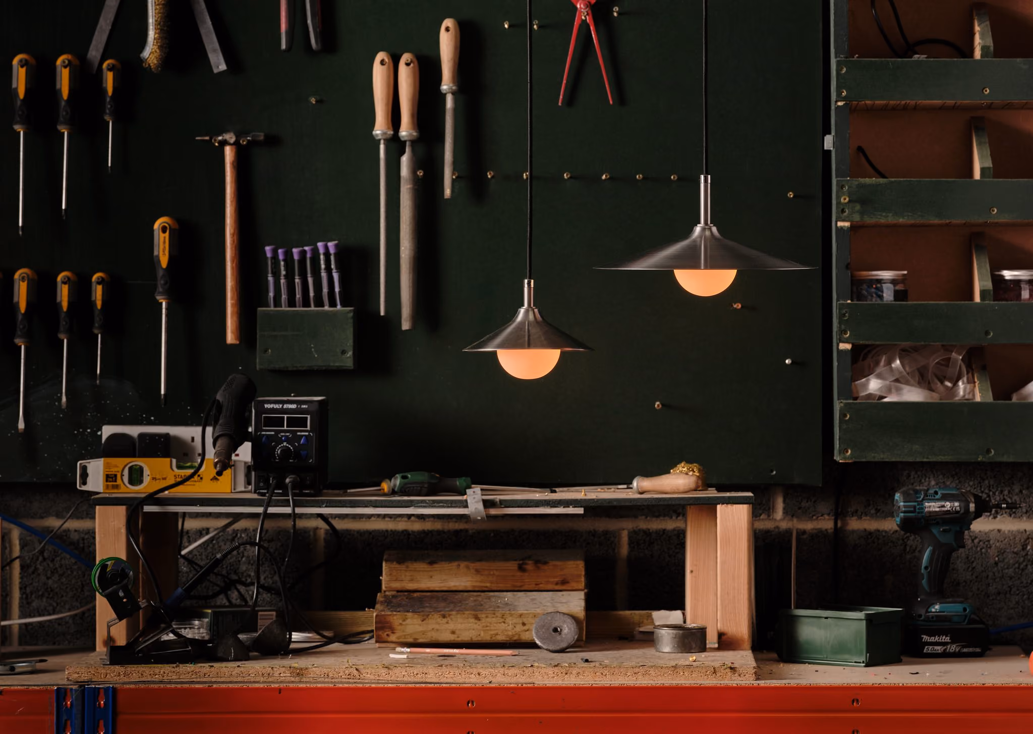 Pair of illuminated Mettle Seren pendants above a workbench and wall of hand tools.