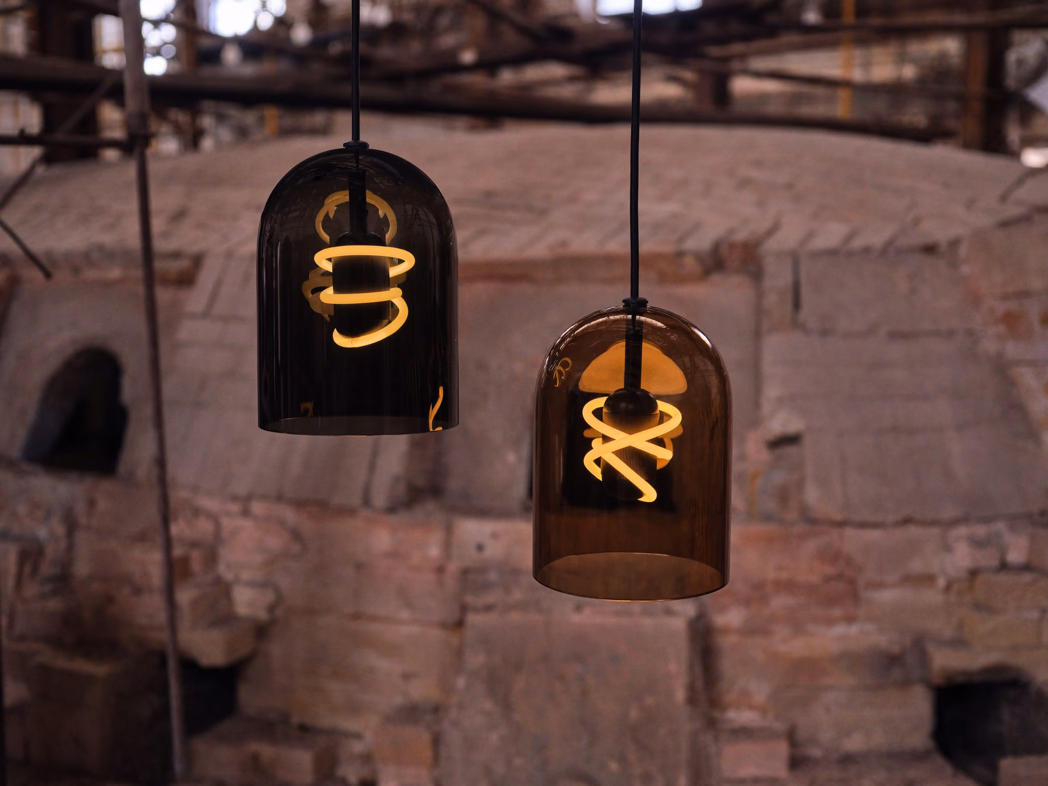 Two BEEM Capo glass pendants with sculptural glowing bulbs against a workshop wall.