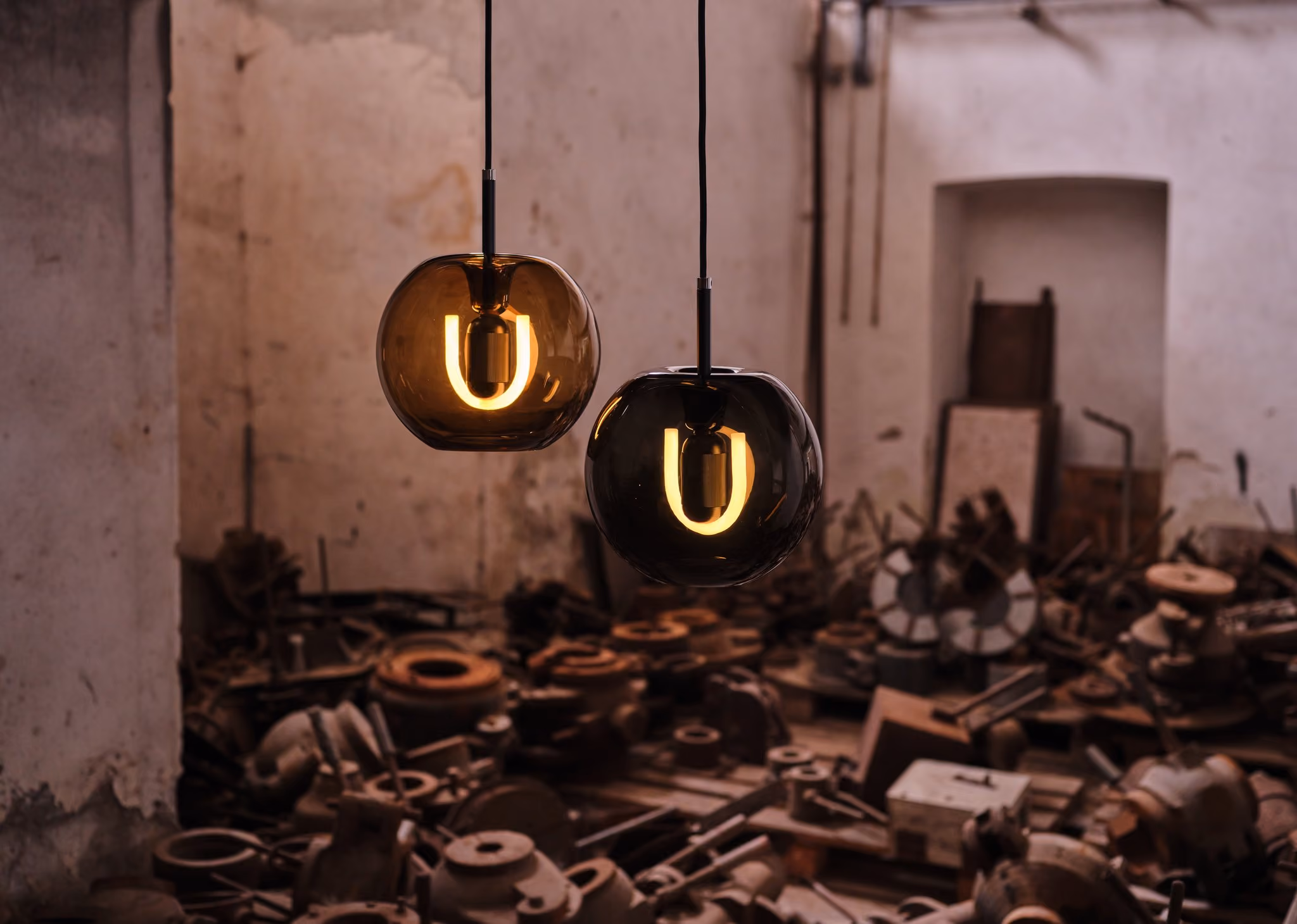 Two BEEM Toru pendants with glowing U-shaped bulbs above metal parts in a workshop.