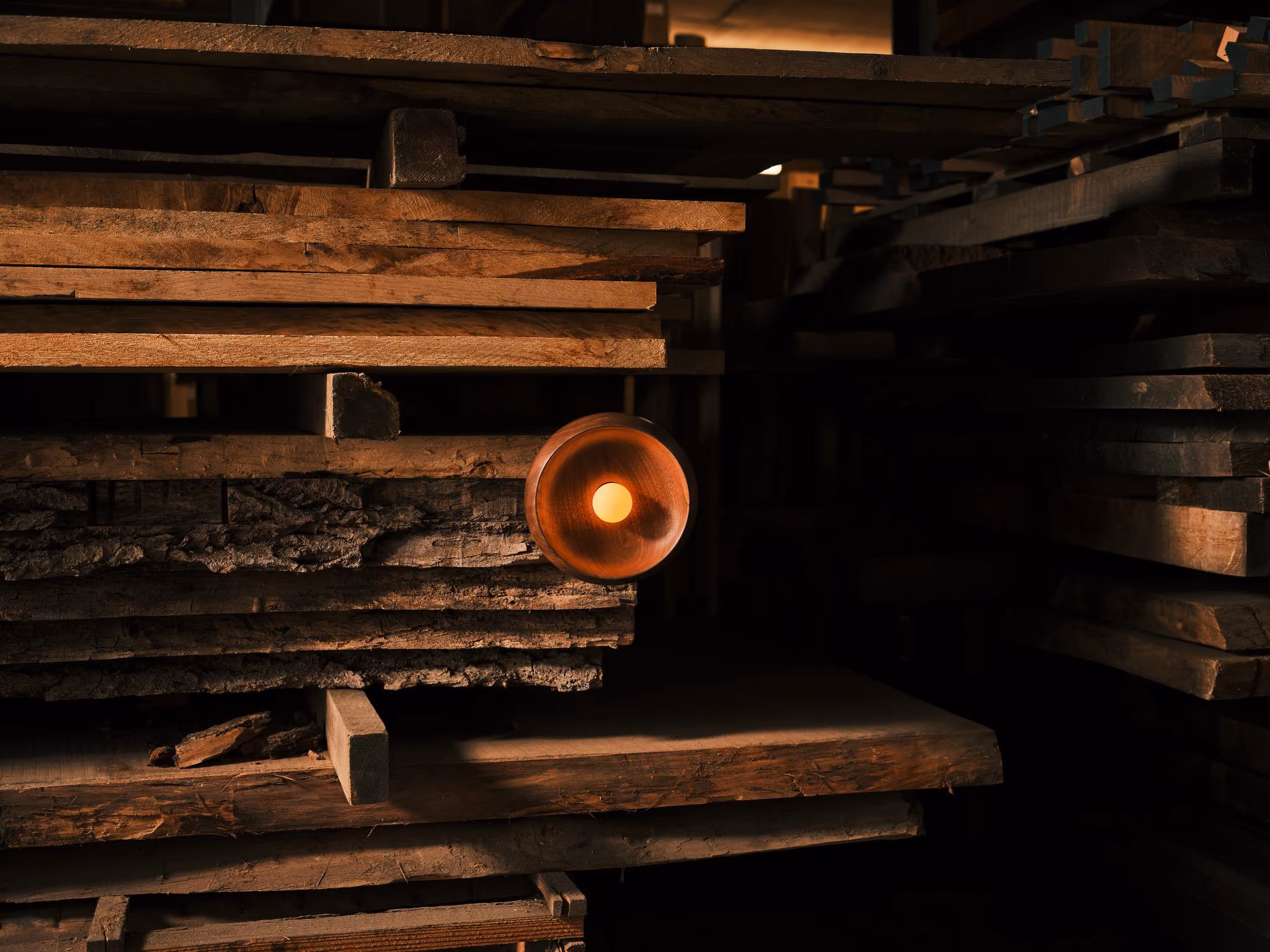 Illuminated Woody Grain walnut wall light mounted among stacked timber boards.