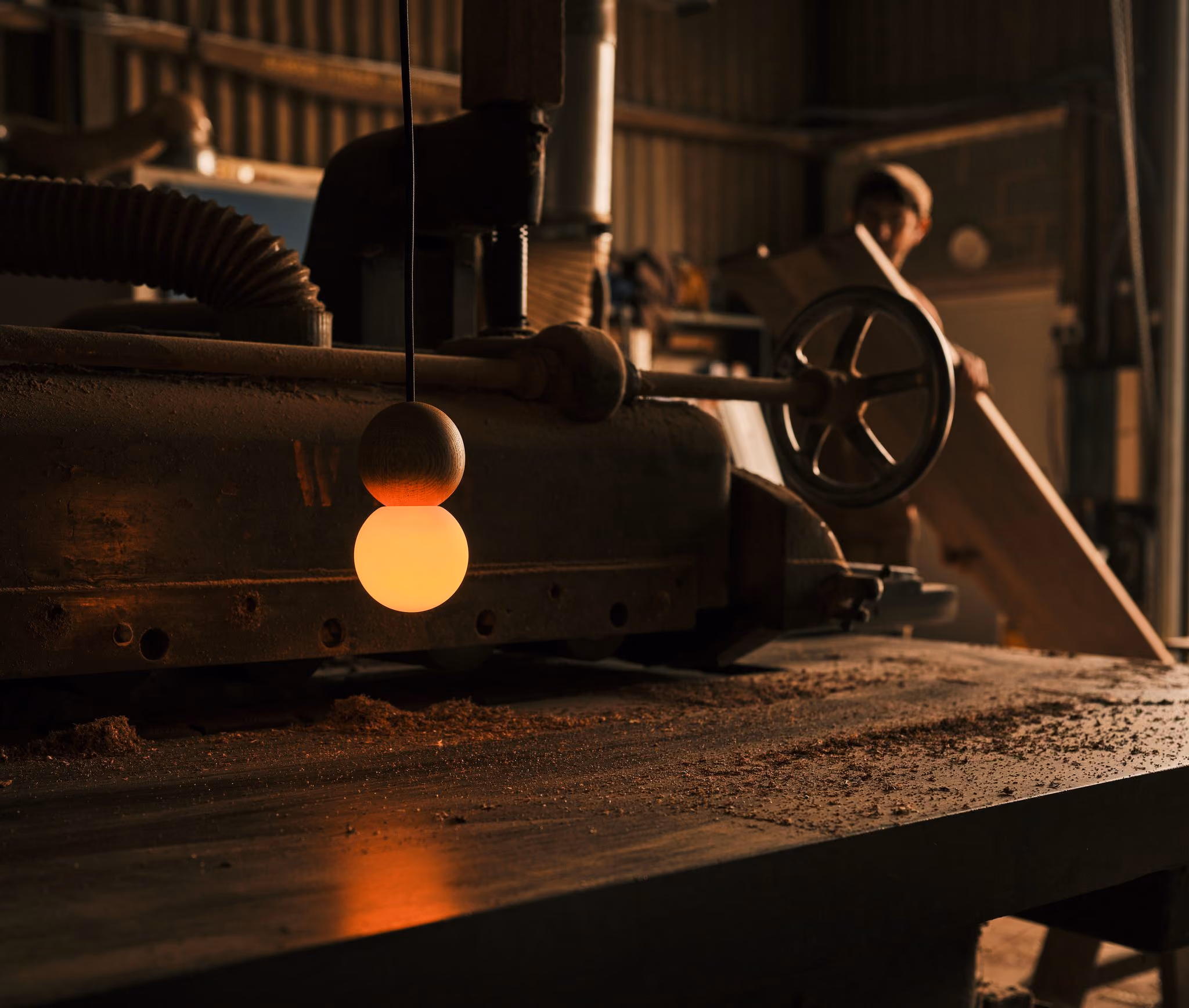 Glowing Woody Duo pendant with a wooden sphere above an opal globe in a woodworking workshop.