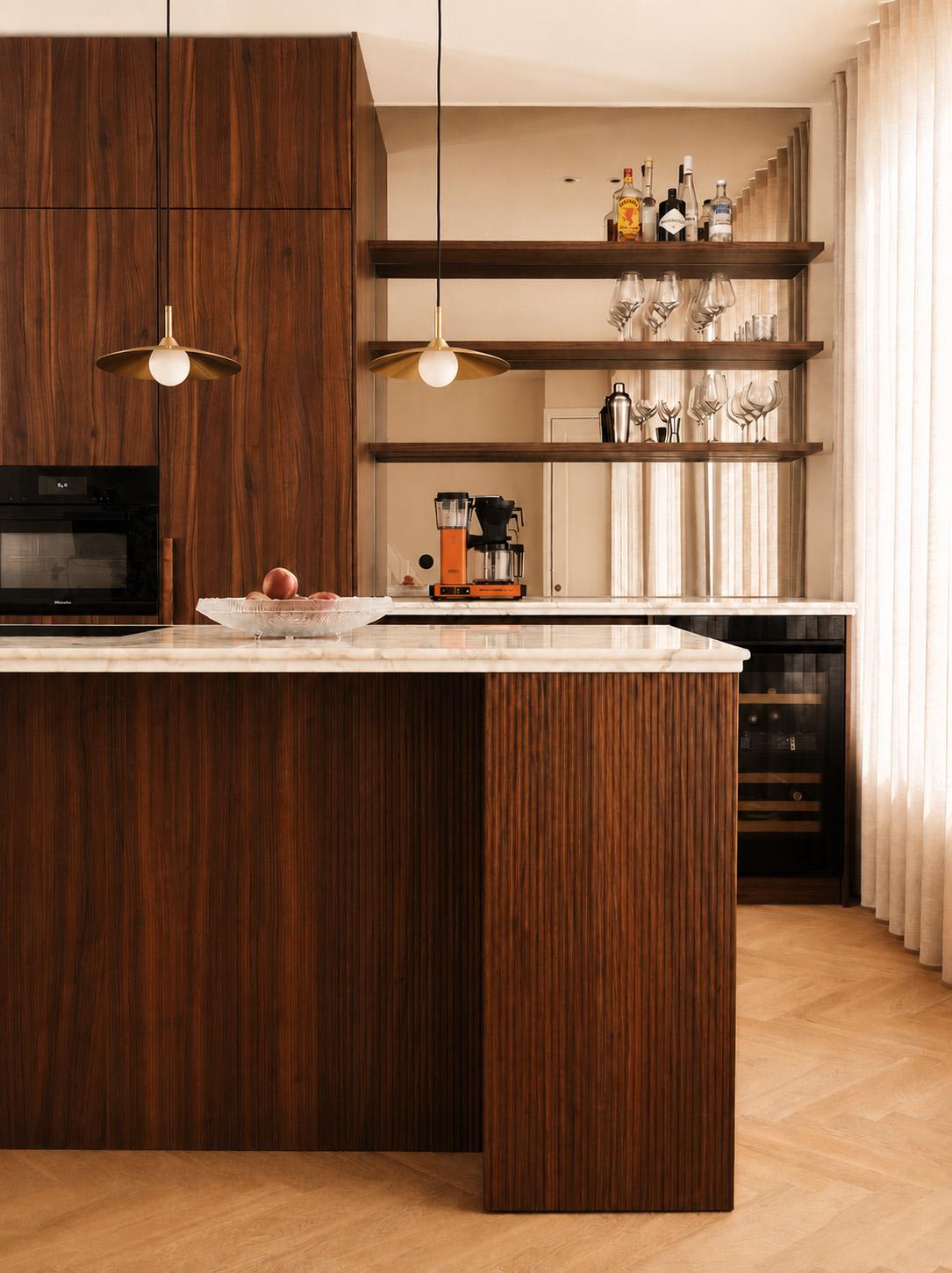 Two brass pendant lights above a marble-topped kitchen island with dark wood cabinetry.
