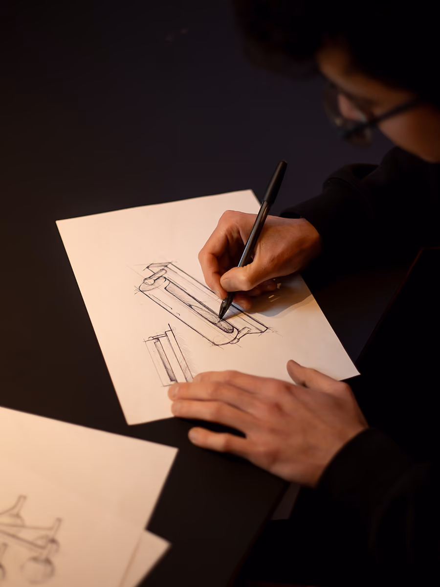 Person sketching technical drawings of a cylindrical mechanical part on white paper using a black pen.