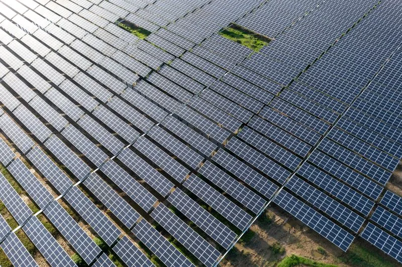 Luftaufnahme eines großen Solarparks mit vielen Solarmodulen und einzelnen freien Flächen mit Gras.