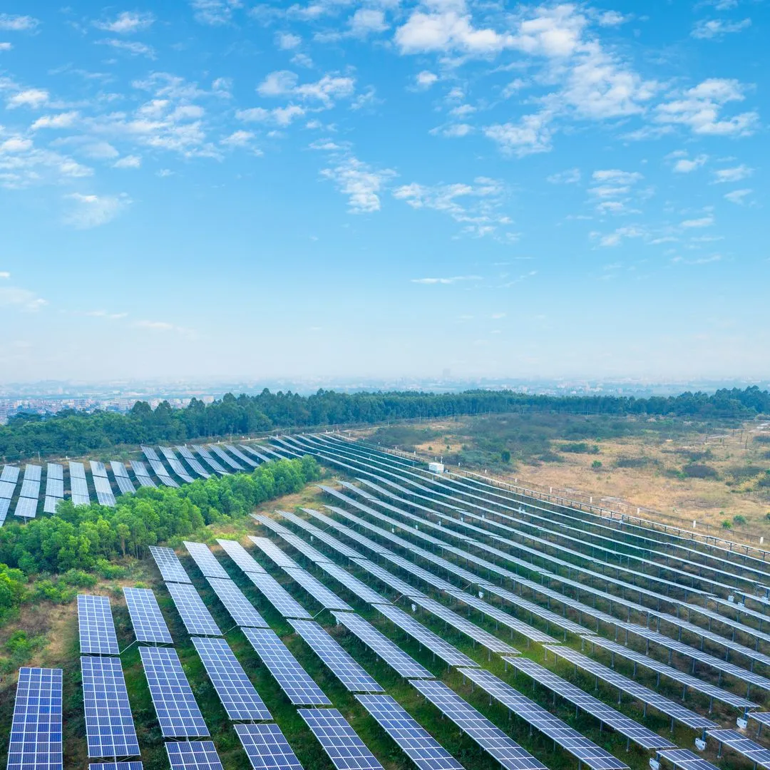 Großes Solarkraftwerk mit Reihen von Solarzellen auf grünem Gras unter blauem Himmel mit vereinzelten Wolken.