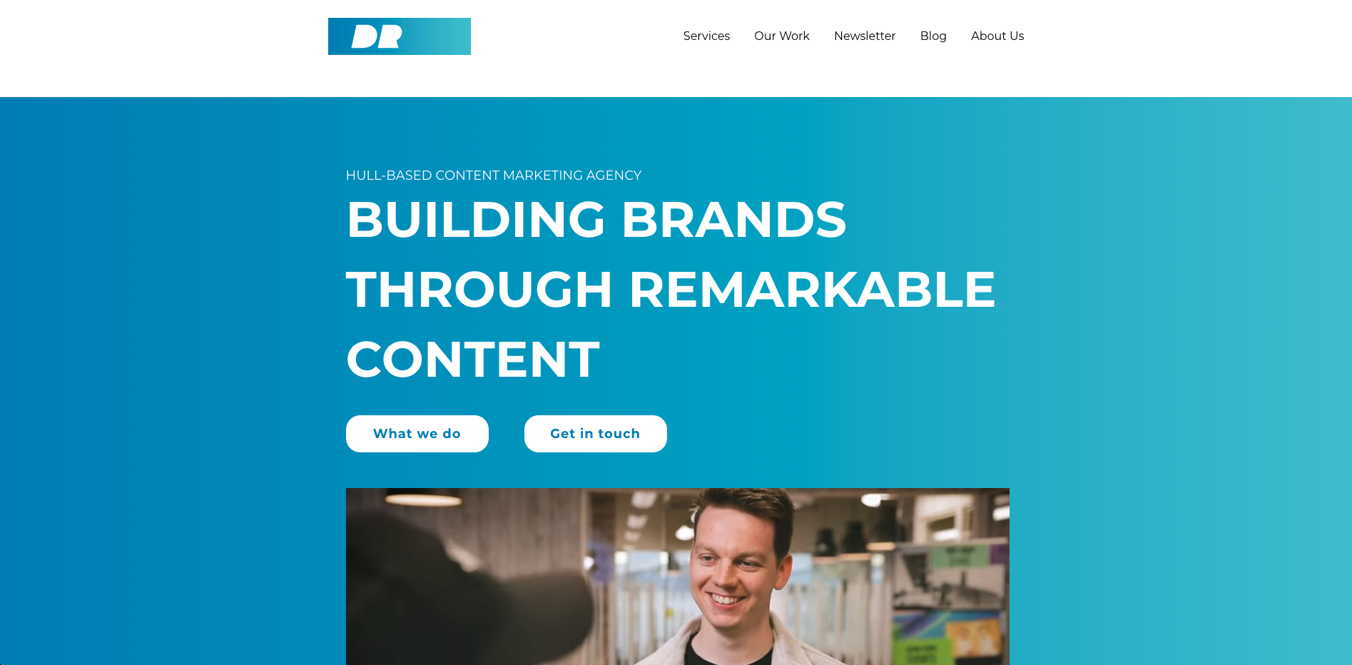 Website header with a blue gradient background showing the text 'Building brands through remarkable content' and two buttons labeled 'What we do' and 'Get in touch', featuring a smiling man in an office setting below.